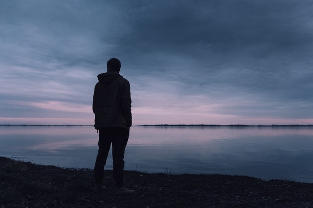 silhouette of a man standing in front of lake as sun has set 