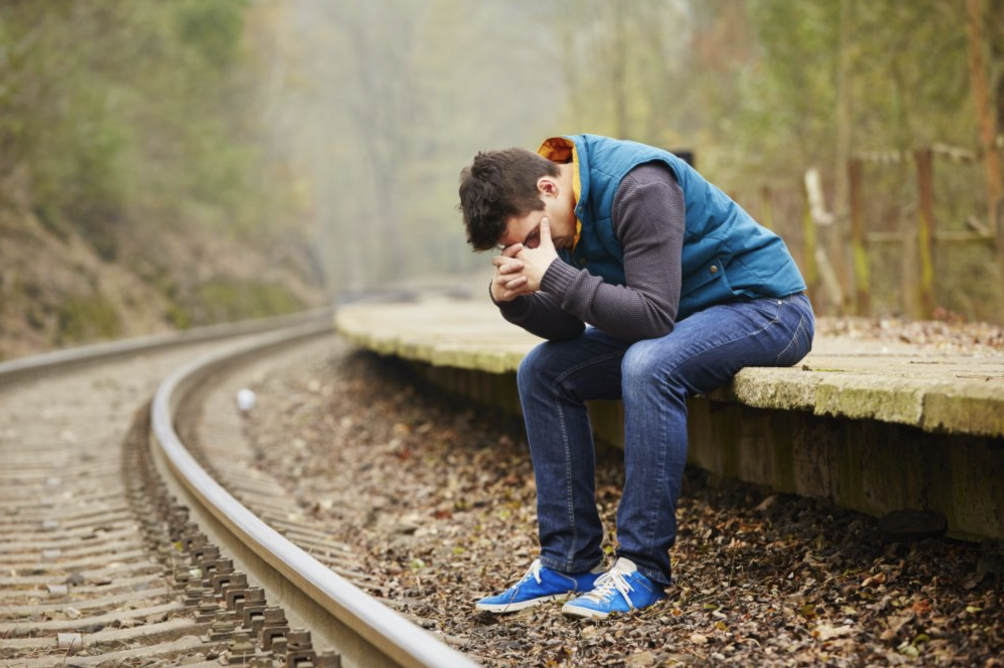Depressed young man sitting alongside railroad track