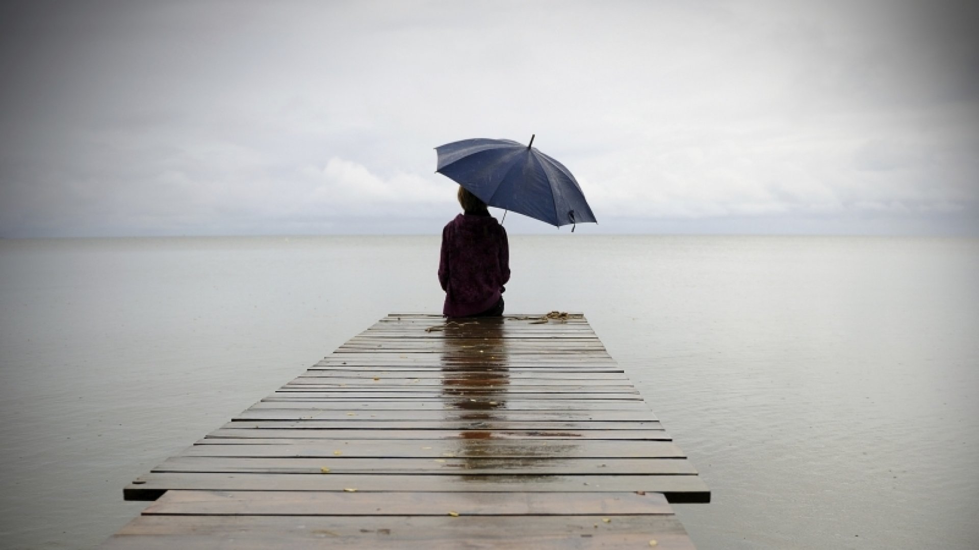 Person sitting on a dock alone in the rain