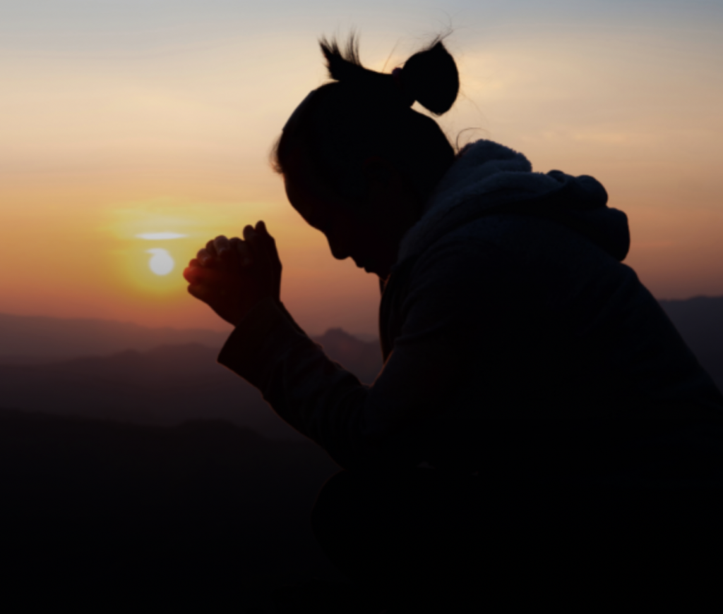 Silhouette of young woman seated in prayerful position at sunset