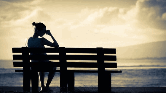 Silhouette of young woman sitting on parkbench contemplating