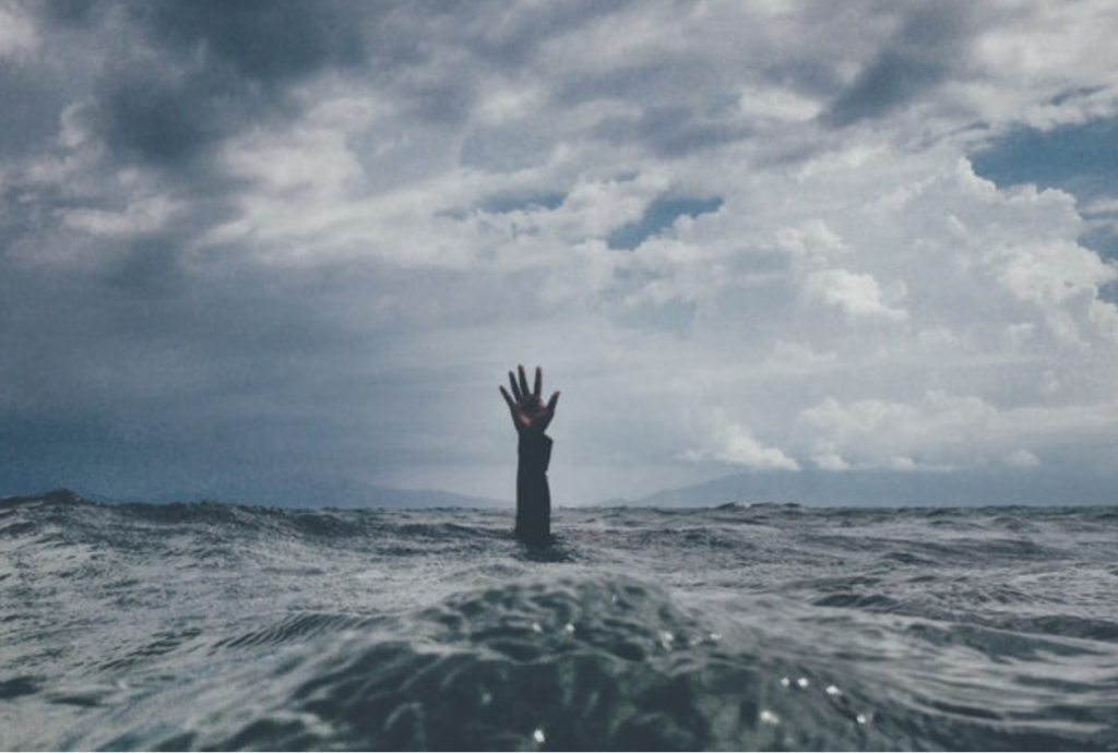 Person's hand above water as they are sinking
