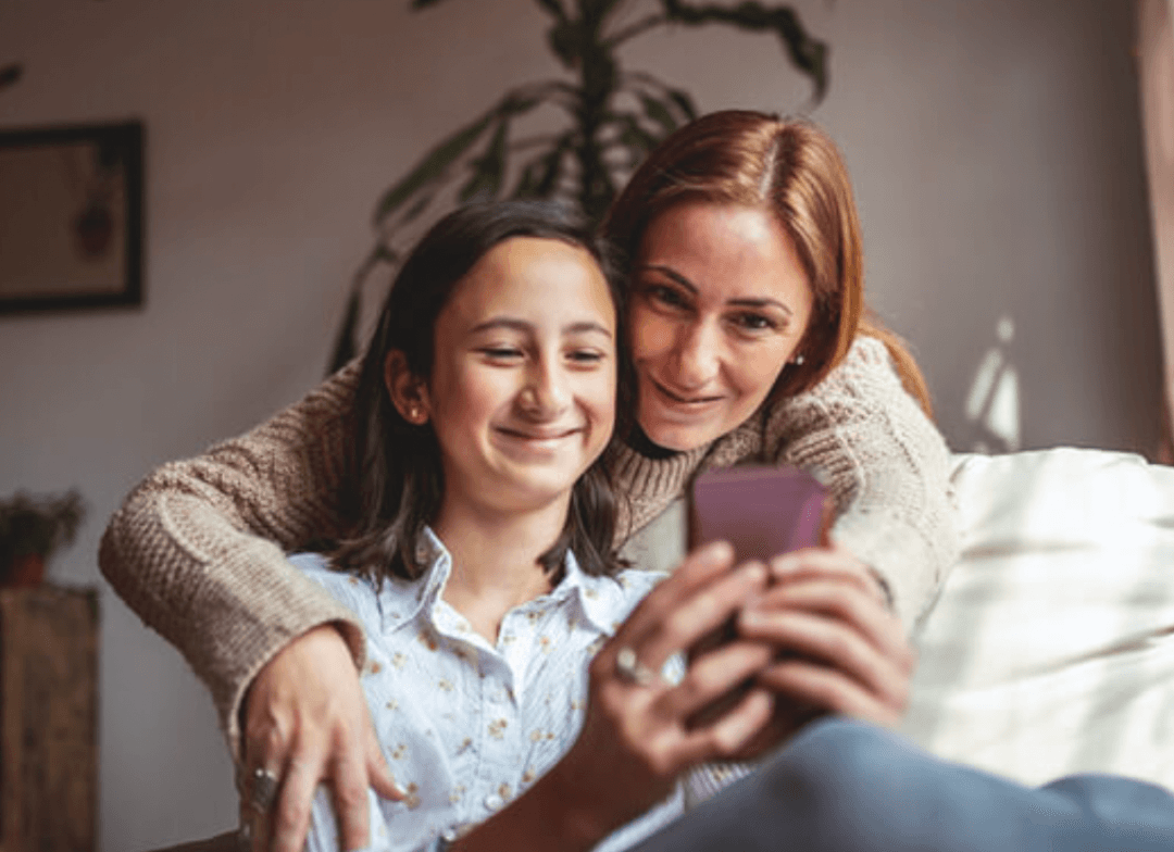 Mom loving on teen daughter and looking at teens' phone together