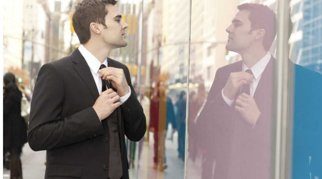 Man arrogantly looking at his reflection in a window as straightens his tie