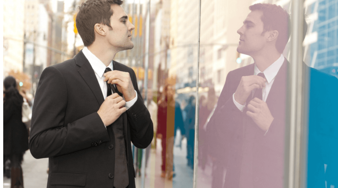 Man arrogantly looking at his reflection in a window as straightens his tie
